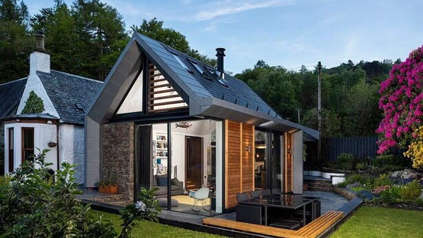 Ein modernes Haus mit Satteldach, großen Glasfenstern und einer Terrassenfläche.