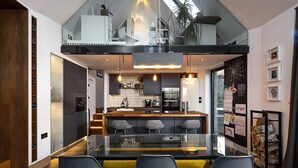 Eine moderne Küche mit Essbereich aus Glas, einer erhöhten Ebene und Blick auf das Wohnzimmer.