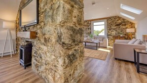 Pared de piedra con un televisor montado, chimenea, sofá y zona de comedor con luz natural.