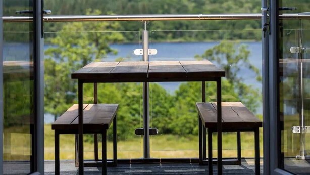 Un balcón con mesa y sillas con vista a un lago y montañas.