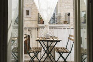 A balcony with a table and chairs, a white curtain, and a building with stone walls and a balcony railing.