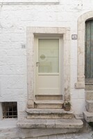 A white door with a glass panel, a small potted plant on the steps, and a number '36' sign on the wall.