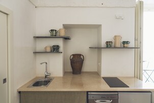 A compact kitchen with a sink, a dishwasher, and shelves holding various kitchenware.