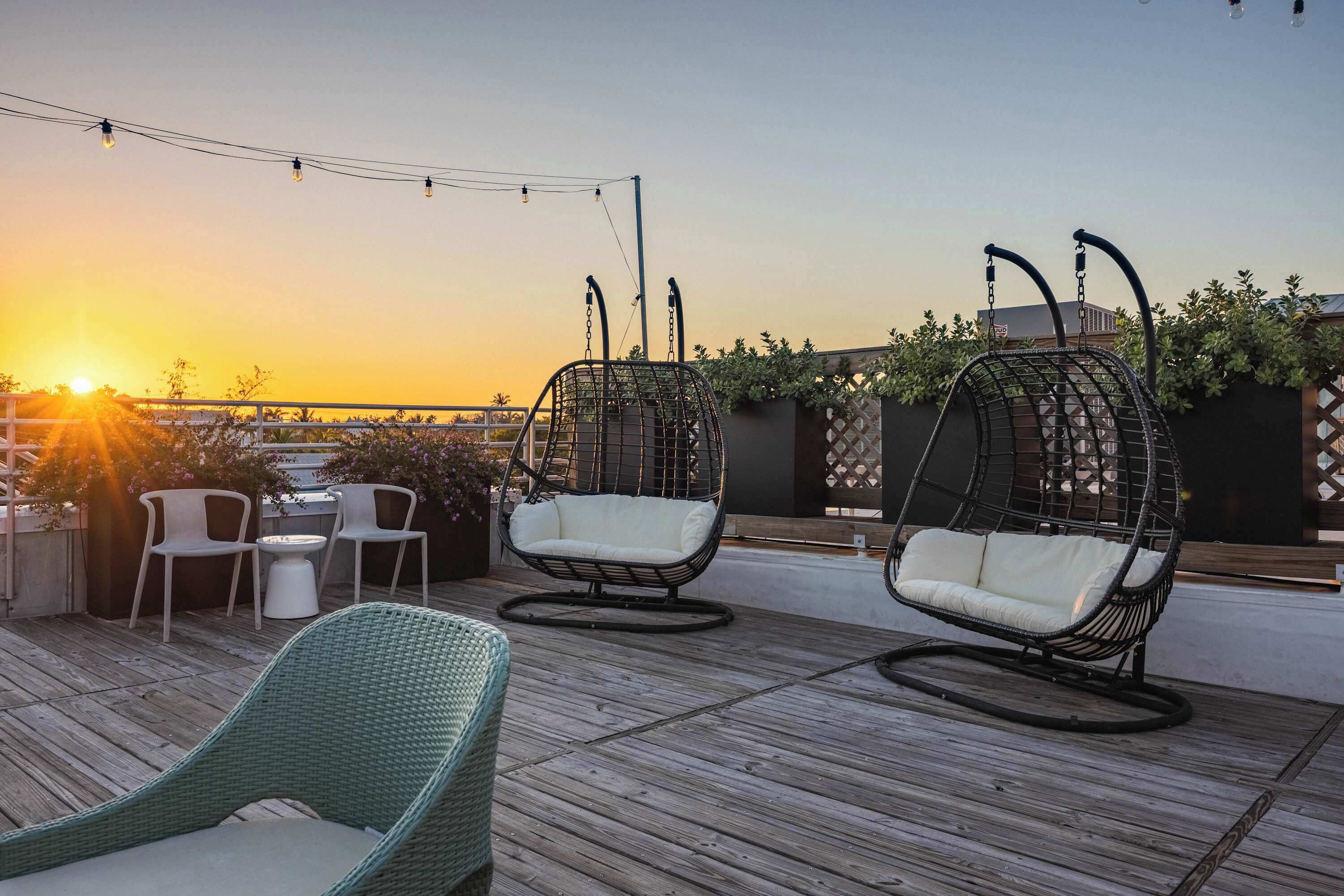 A rooftop patio with wicker chairs, a table, and string lights.