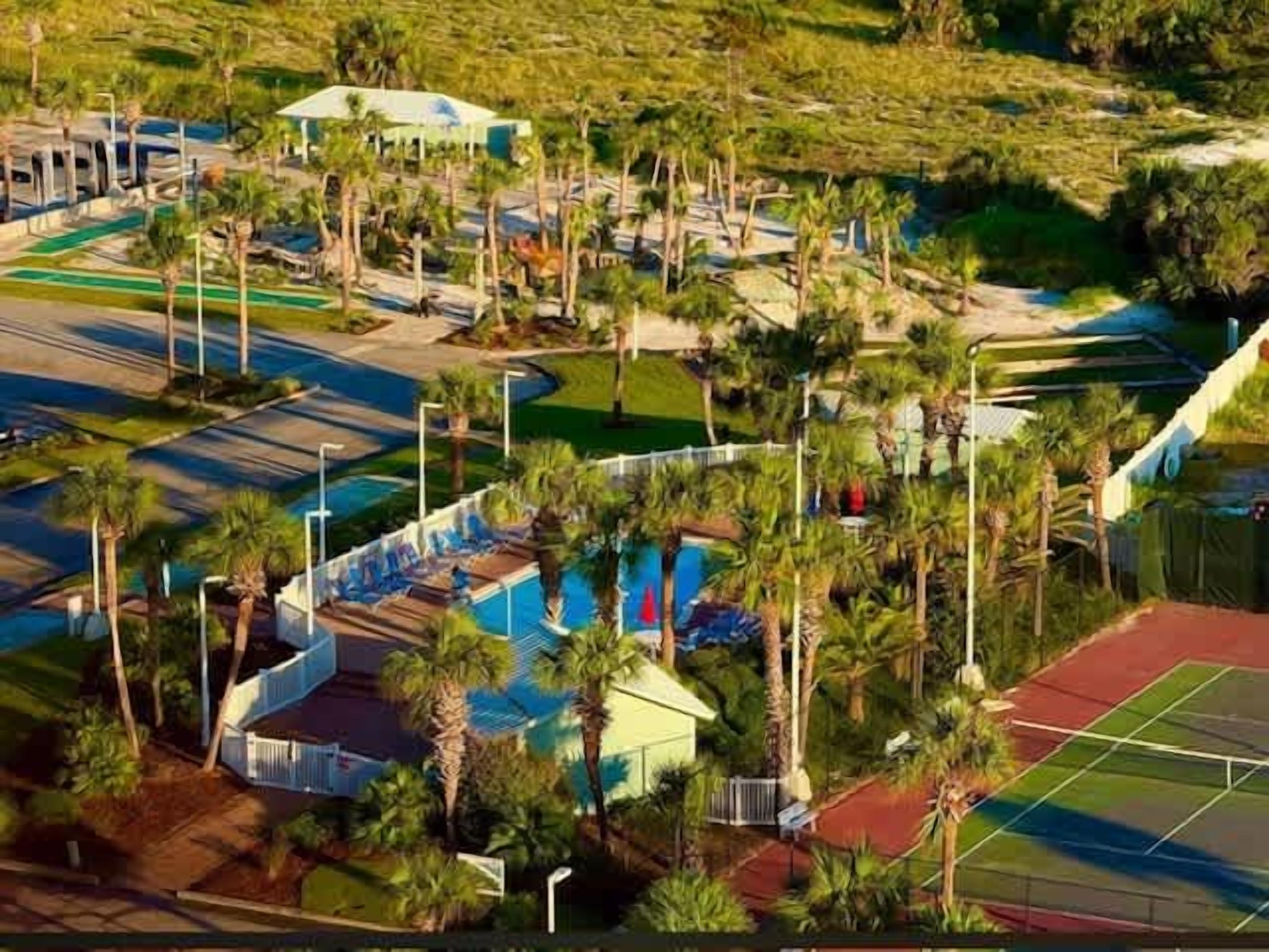 An aerial view of a resort with multiple tennis courts, a swimming pool, and palm trees.