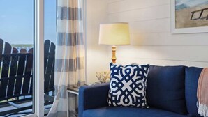 Une pièce avec un canapé bleu, un coussin à motifs, une lampe et un tableau représentant une scène de plage.