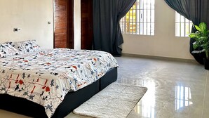 A bedroom with a large bed, a small rug, a potted plant, and a window with curtains.