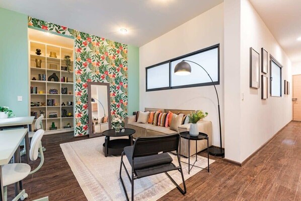 A modern living room with a sofa, coffee table, and chairs, a bookshelf, and a decorative wall with floral wallpaper.