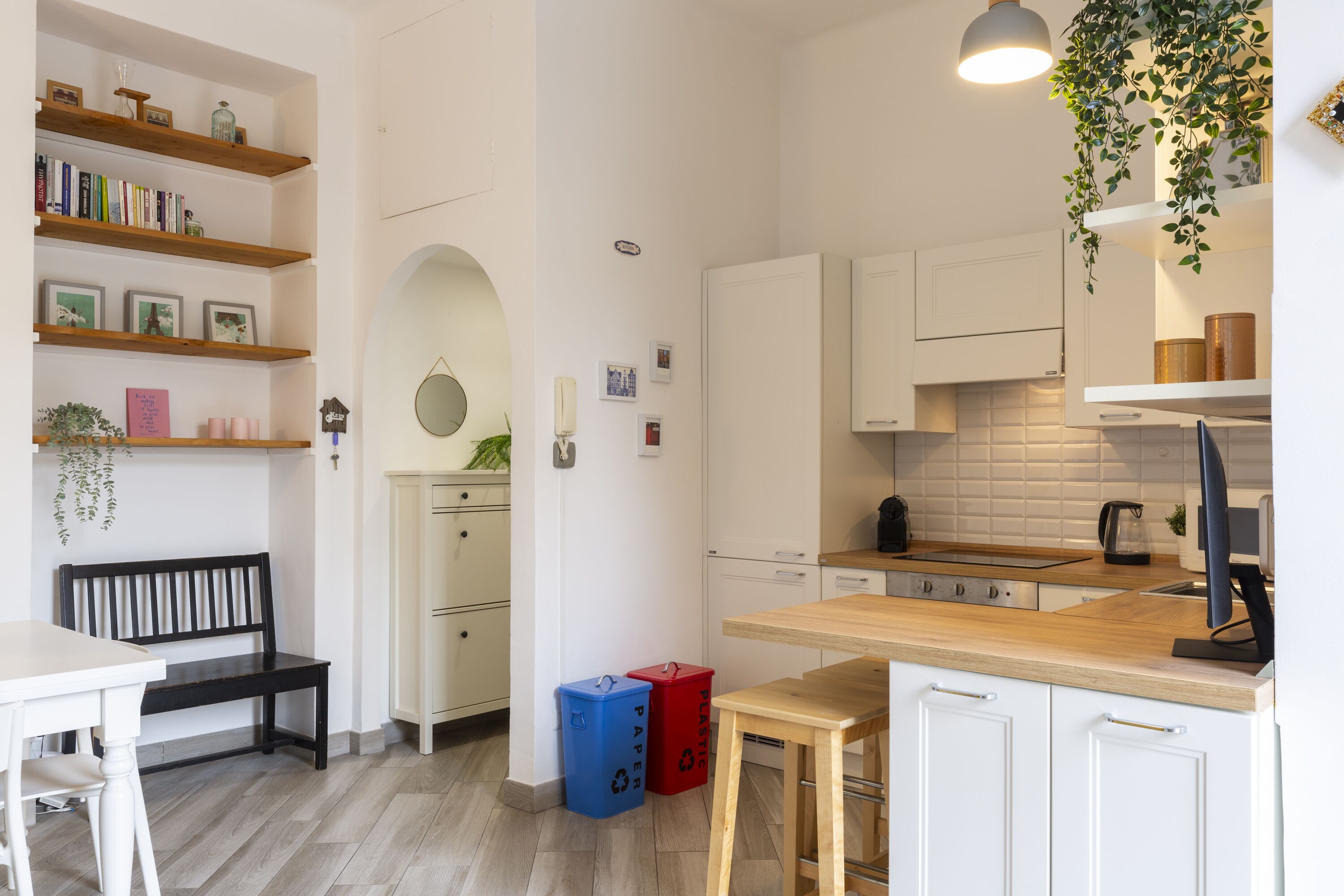 Une cuisine moderne avec des meubles blancs, des étagères en bois et un coin repas doté d’une banquette.