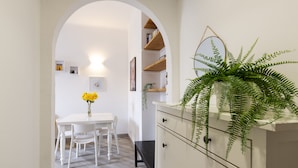 A dining area with a white table and chairs, a white cabinet with drawers, and a plant on the cabinet. - nota-Mi - Mezzofanti TRE PONTI (Milan)
