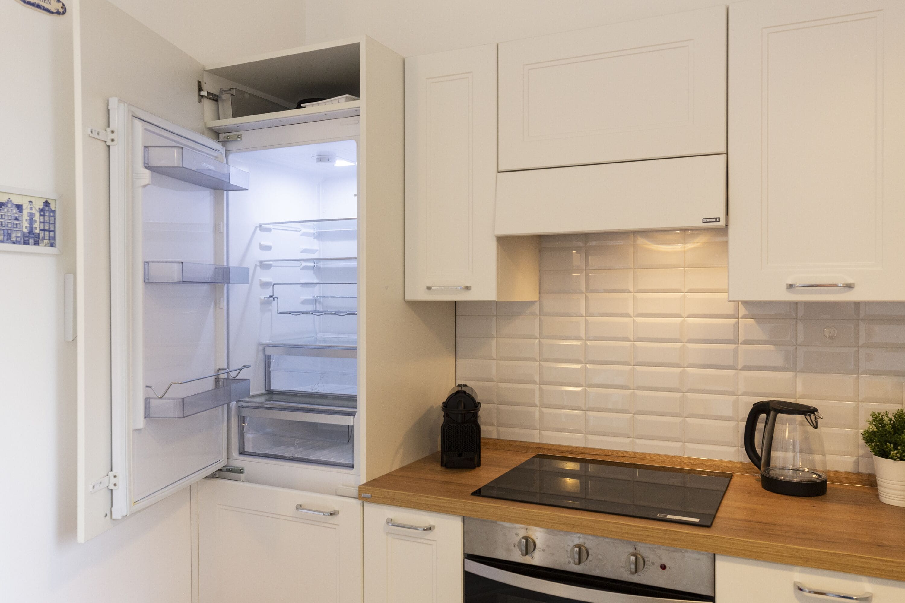 A modern kitchen with white cabinets, a built-in oven, a black coffee maker, and a wooden countertop.