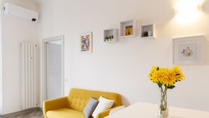 A modern living room with a yellow sofa, a white table, and a vase of yellow flowers. - nota-Mi - Mezzofanti TRE PONTI (Milan)