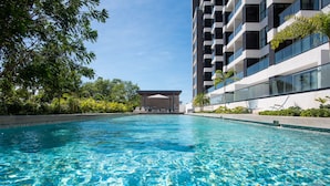 A swimming pool with clear blue water, surrounded by greenery and modern buildings. - New Deluxe Unit, Signature Condominium by The Harbor (Mérida)
