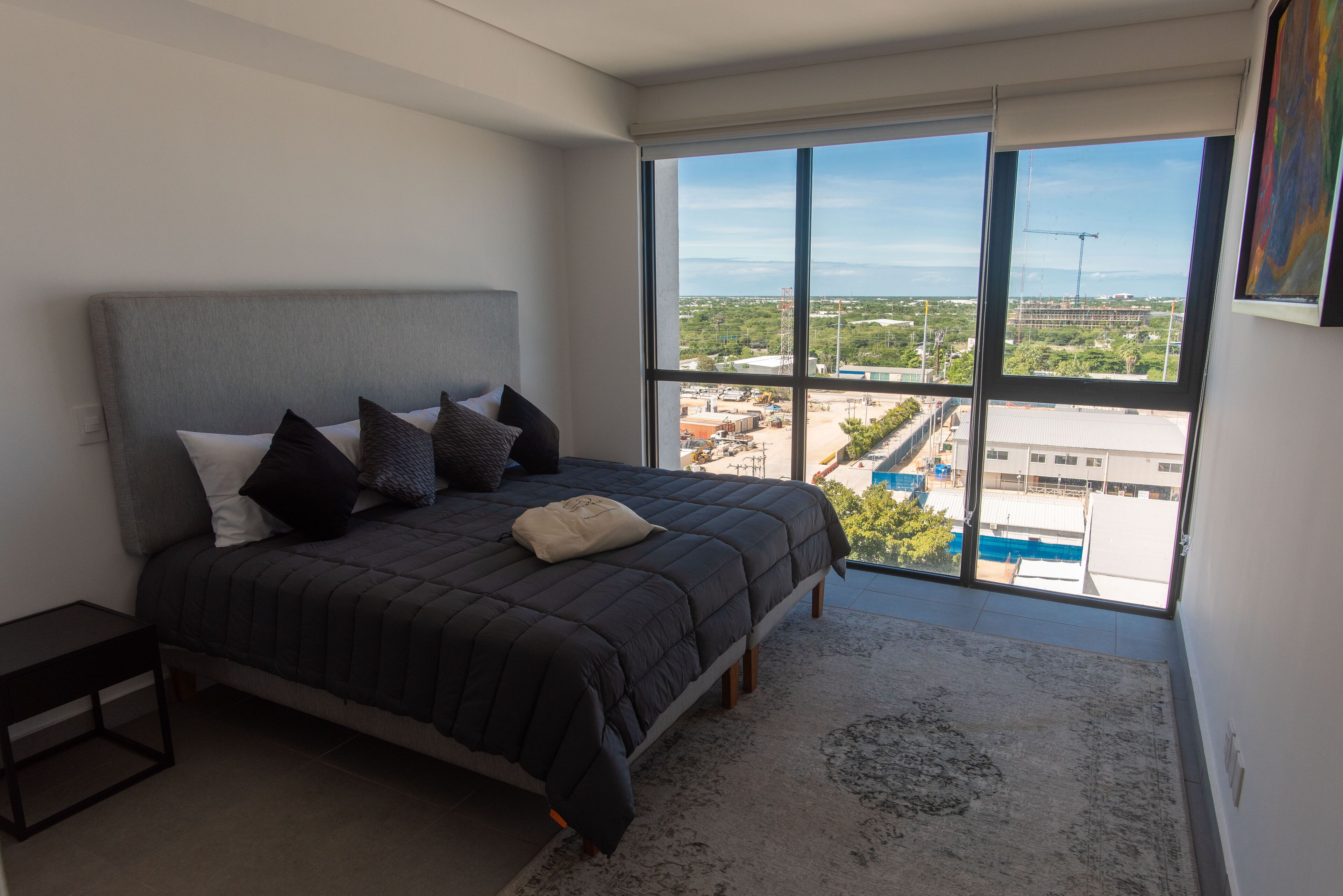 A bedroom with a large bed, a nightstand, and a view of a construction site through a large window.