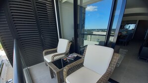 A balcony with wicker chairs and a small table, overlooking a parking area and buildings. - New Deluxe Unit, Signature Condominium by The Harbor (Mérida)