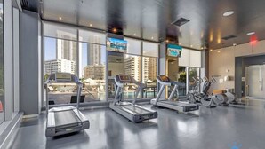 Et moderne fitnesscenter med løbebånd og spinningcykler, store vinduer med udsigt over byen og et rent, slebet gulv.