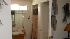 A bedroom with a bed, a bathroom with a sink and mirror, and a door leading to another room.