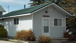 A small, single-story cabin with a green roof, a white door, and a sign above the door indicating it is number 240, Pine Cone Cabin.