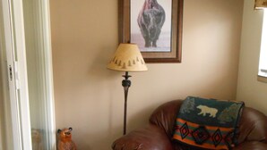 A living room with a brown leather sofa, a lamp, a bear figurine, a rug, and a framed picture of a bear on the wall.