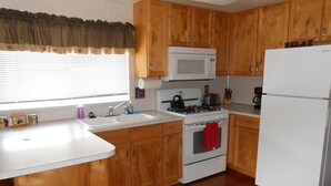 A kitchen with wooden cabinets, a white stove, a microwave, a sink, and a refrigerator.