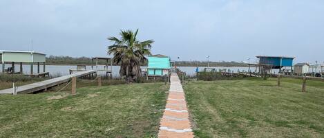 Un sendero que conduce a una zona de playa con una palmera, un pabellón y un pequeño edificio azul.