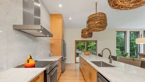 Een moderne keuken met marmeren werkbladen, roestvrijstalen apparatuur, houten kasten en een groot raam met uitzicht op de omgeving.