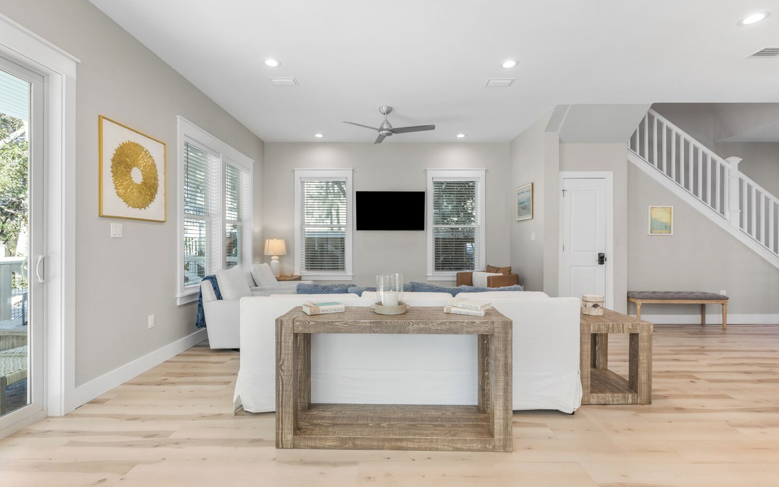 A spacious living room with a large window, a ceiling fan, and a staircase leading to an upper level.