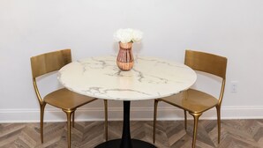 Ein runder Tisch mit Marmorplatte, zwei goldene Stühle und eine Vase mit weißen Blumen.