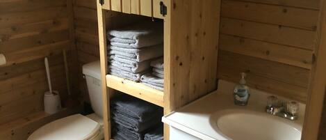 Un baño pequeño de madera con un inodoro, un lavabo y un estante con toallas dobladas.