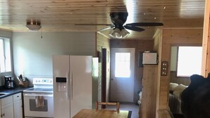 Un intérieur en bois comprenant une table à manger, des bancs, un réfrigérateur, une cuisinière et un ventilateur de plafond.