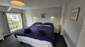 Una camera da letto ordinata con un letto grande, due comodini, una finestra con tende e un quadro appeso al muro.
