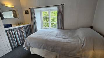 Une chambre avec un grand lit, une fenêtre avec des rideaux, un lavabo et un miroir.
