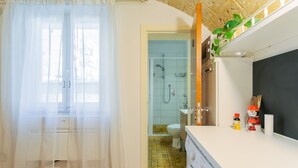 A bathroom with a shower, toilet, and sink. There is a curtain, a plant, and a shelf with toiletries.