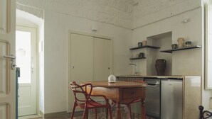 A compact kitchen with a dining table, chairs, a dishwasher, and shelves with decorative items.