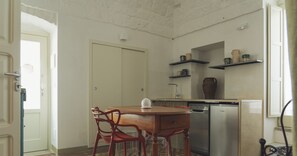 A compact kitchen with a dining table, chairs, a dishwasher, and shelves with decorative items.