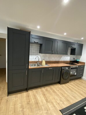 Una cocina moderna con armarios oscuros, encimera de madera, lavadora integrada y salpicadero de azulejos.