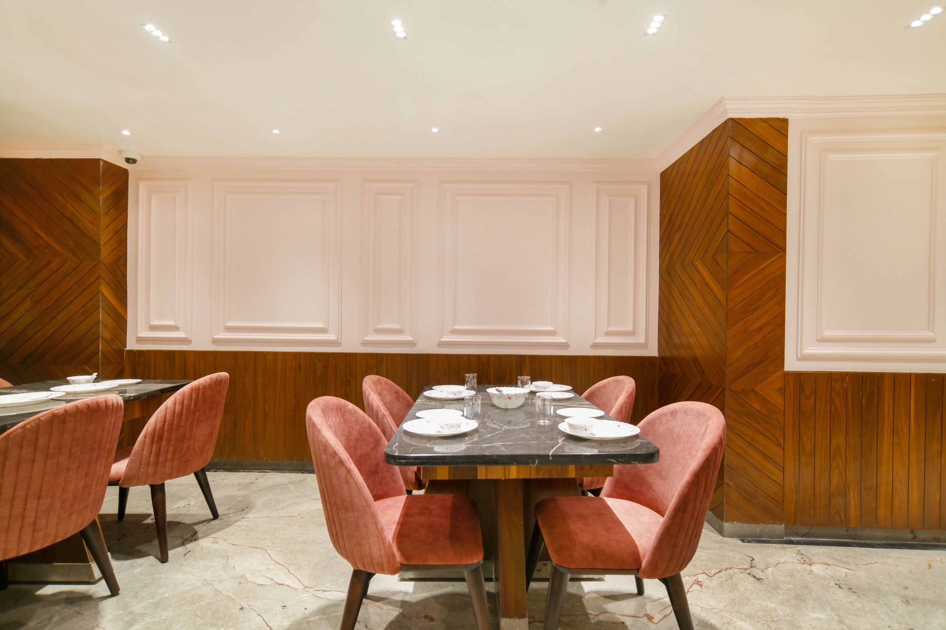 A conference room with a rectangular table, six pink upholstered chairs, and a marble floor.