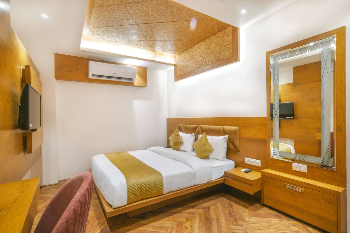 Una habitación de hotel moderna con una cama de madera, un espejo grande, un zapatero y un equipo de aire acondicionado integrado.