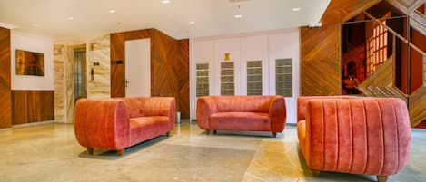 Un hall con tres sofás rojos y cómodos, suelo de mármol y pared de madera con un diseño geométrico.