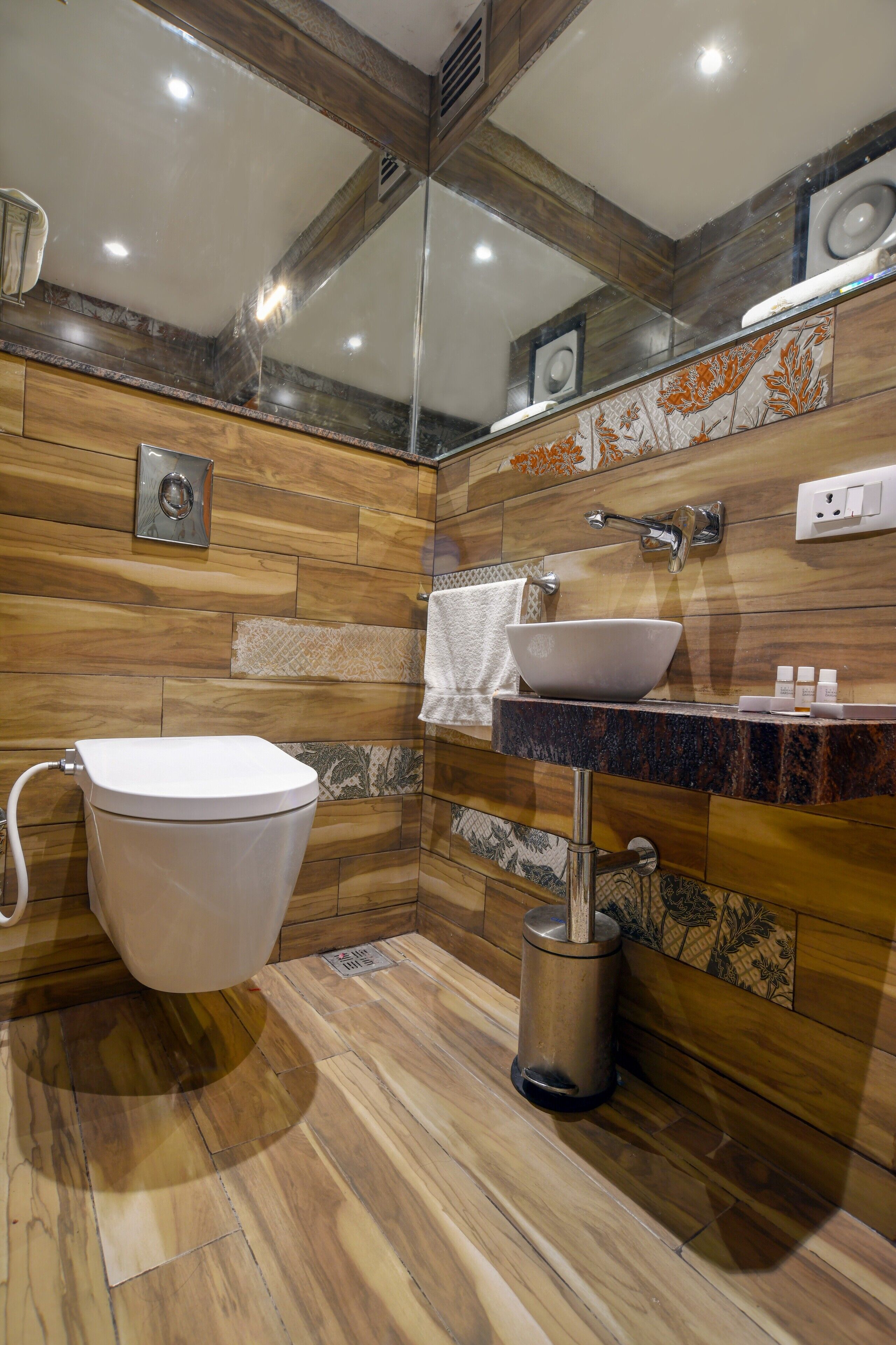 A modern bathroom with a wooden floor, a white toilet, a vessel sink, and a mirror.