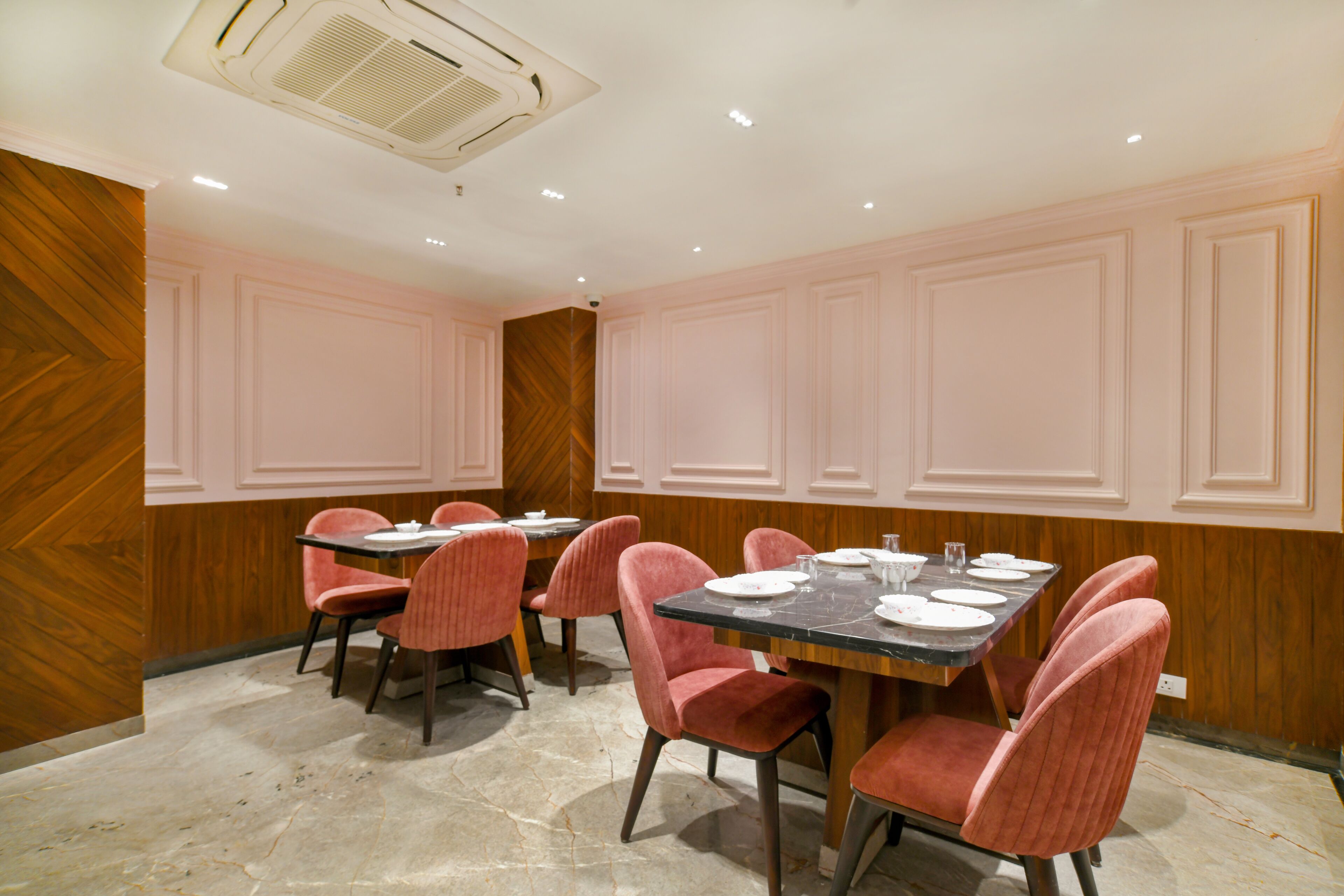 A dining area with a table set for four, surrounded by pink upholstered chairs, wooden panel walls, and a marble floor.