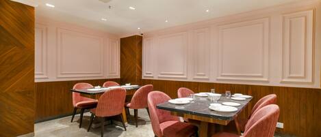 A dining area with a table set for four, surrounded by pink upholstered chairs, wooden panel walls, and a marble floor.