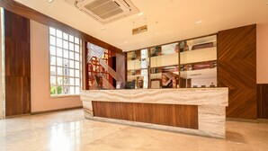 A reception area with a marble counter, wooden paneling, and a large window. - Hathili Hotel and Restaurant (Ujjain)