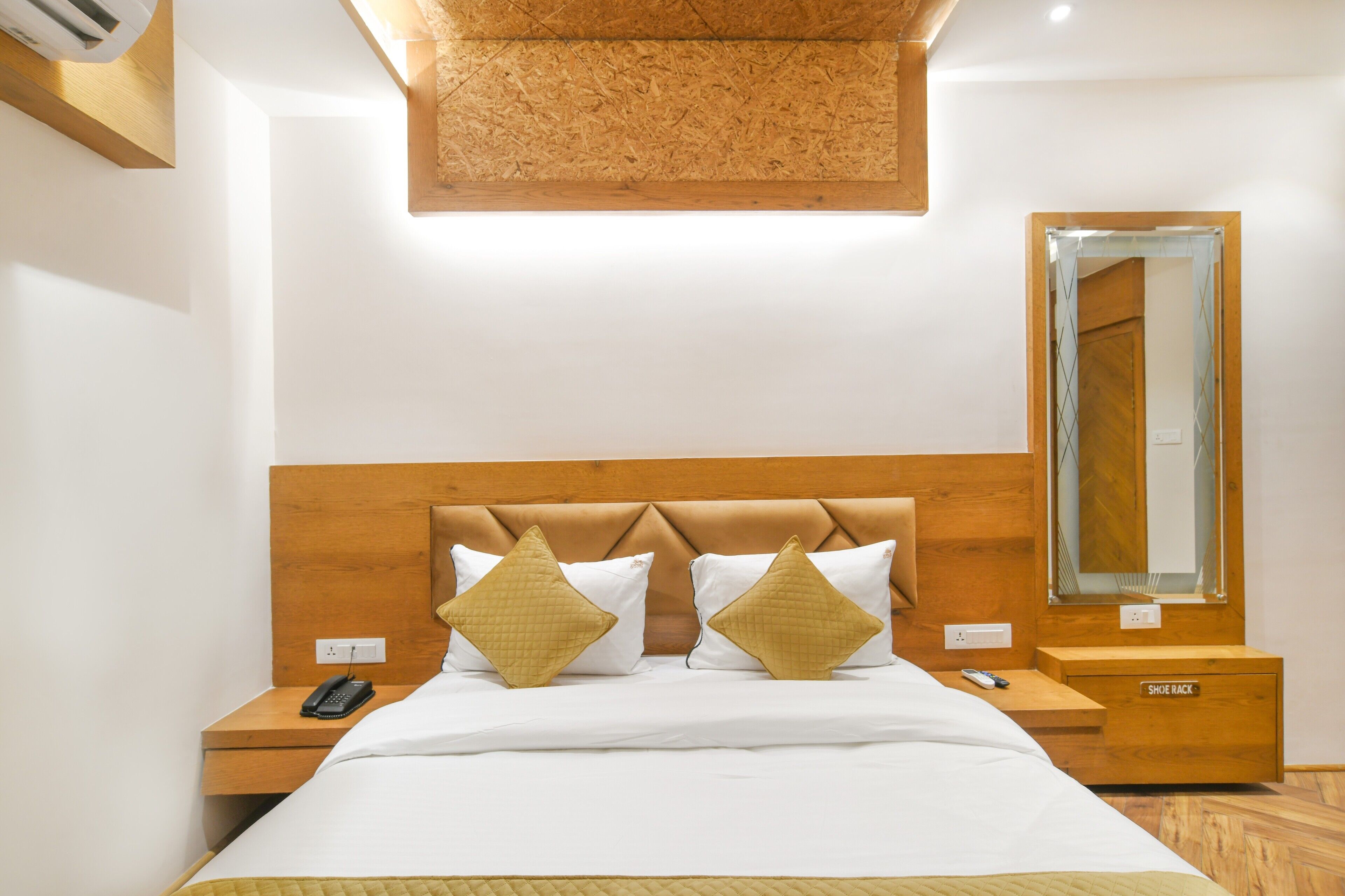 Une chambre d’hôtel avec une tête de lit en bois, deux tables de chevet, un miroir et un porte-chaussures.