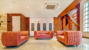 A lobby with three plush red sofas, a marble floor, a wooden wall with a geometric pattern, and a staircase with wooden railings. - Hathili Hotel and Restaurant (Ujjain)