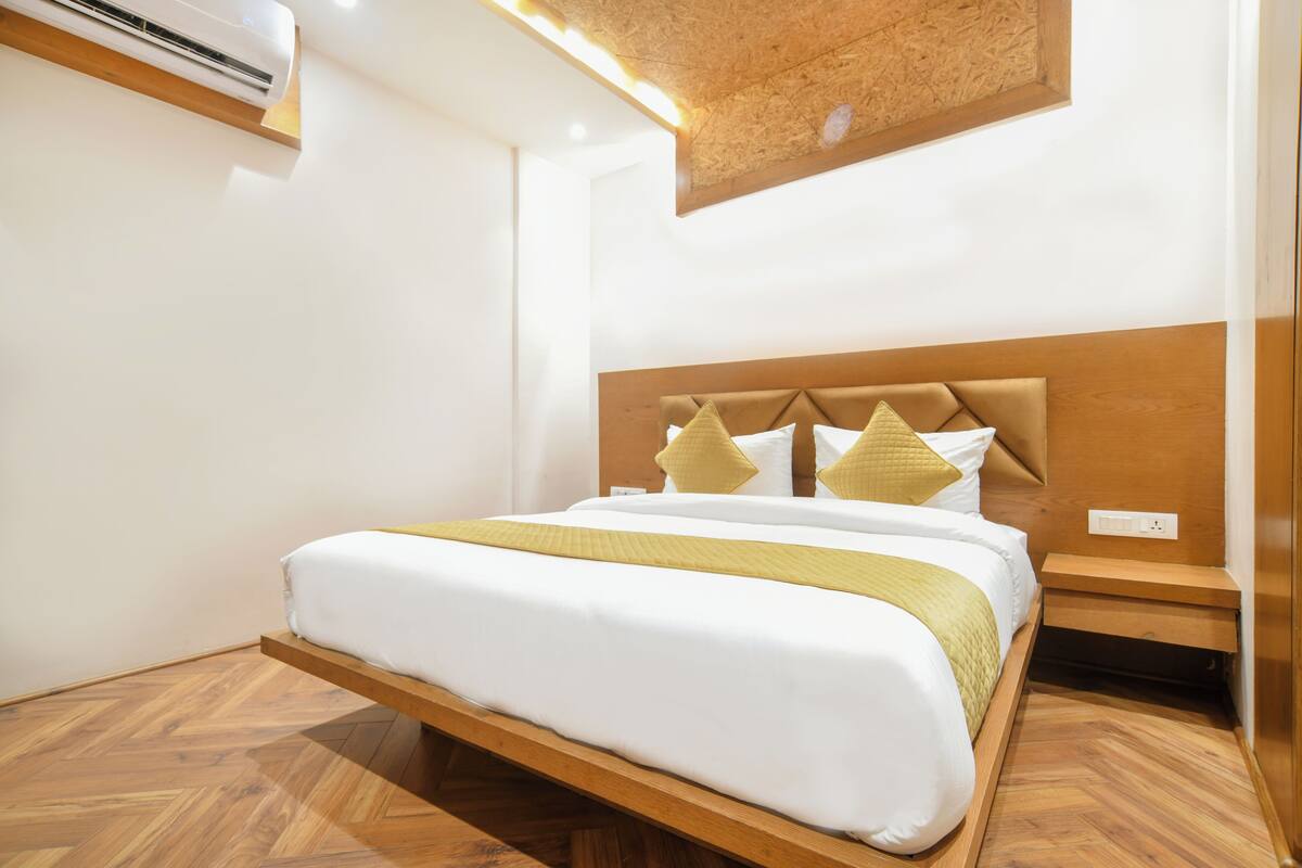 Una habitación de hotel moderna con estructura de cama de madera, cabecera con almohadones decorativos y estante empotrado.