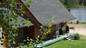 A wooden cabin with a porch, a small deck, and a view of a lake. - Jim's Cottage (Egan-Sud)
