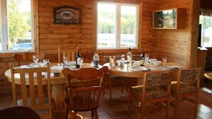 A wooden cabin interior with a dining table set for six, surrounded by wooden chairs. - Jim's Cottage (Egan-Sud)