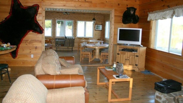 A cabin interior with a dining area, a television, and a bear mounted on the wall. - Jim's Cottage (Egan-Sud)