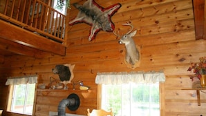 A cabin interior with wooden walls, a wooden staircase, a fireplace, and mounted animal heads. - Jim's Cottage (Egan-Sud)